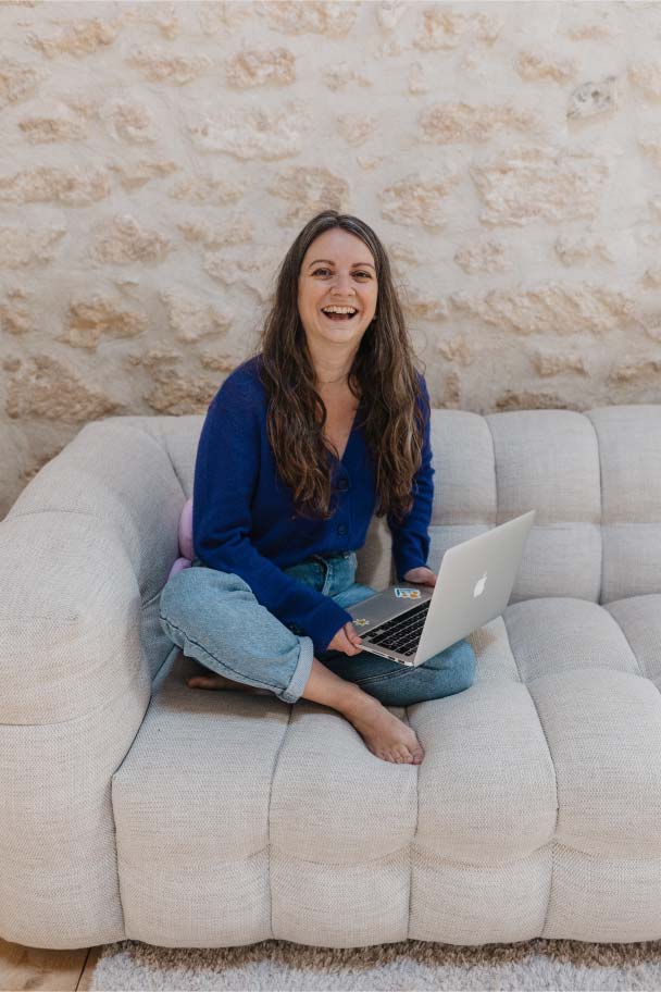 Steffi, créatrice de site web éco-responsable, travaille assise en tailleur sur un canapé